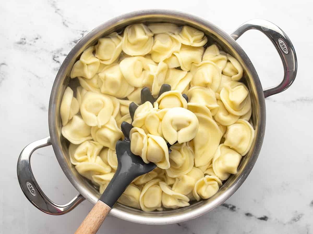 Cooked tortellini in a pot with a pasta fork lifting some.