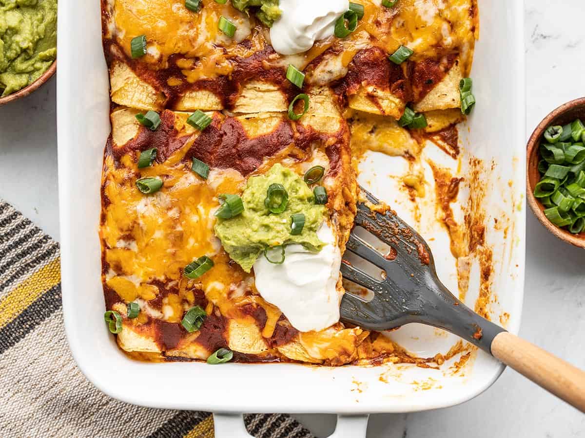 Close up of enchiladas being scooped out of the casserole dish