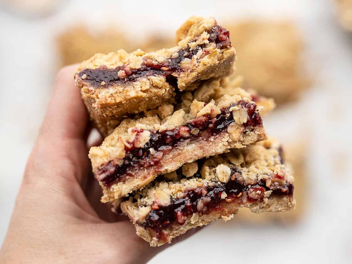 A hand holding a stack of raspberry oatmeal bars close to the camera
