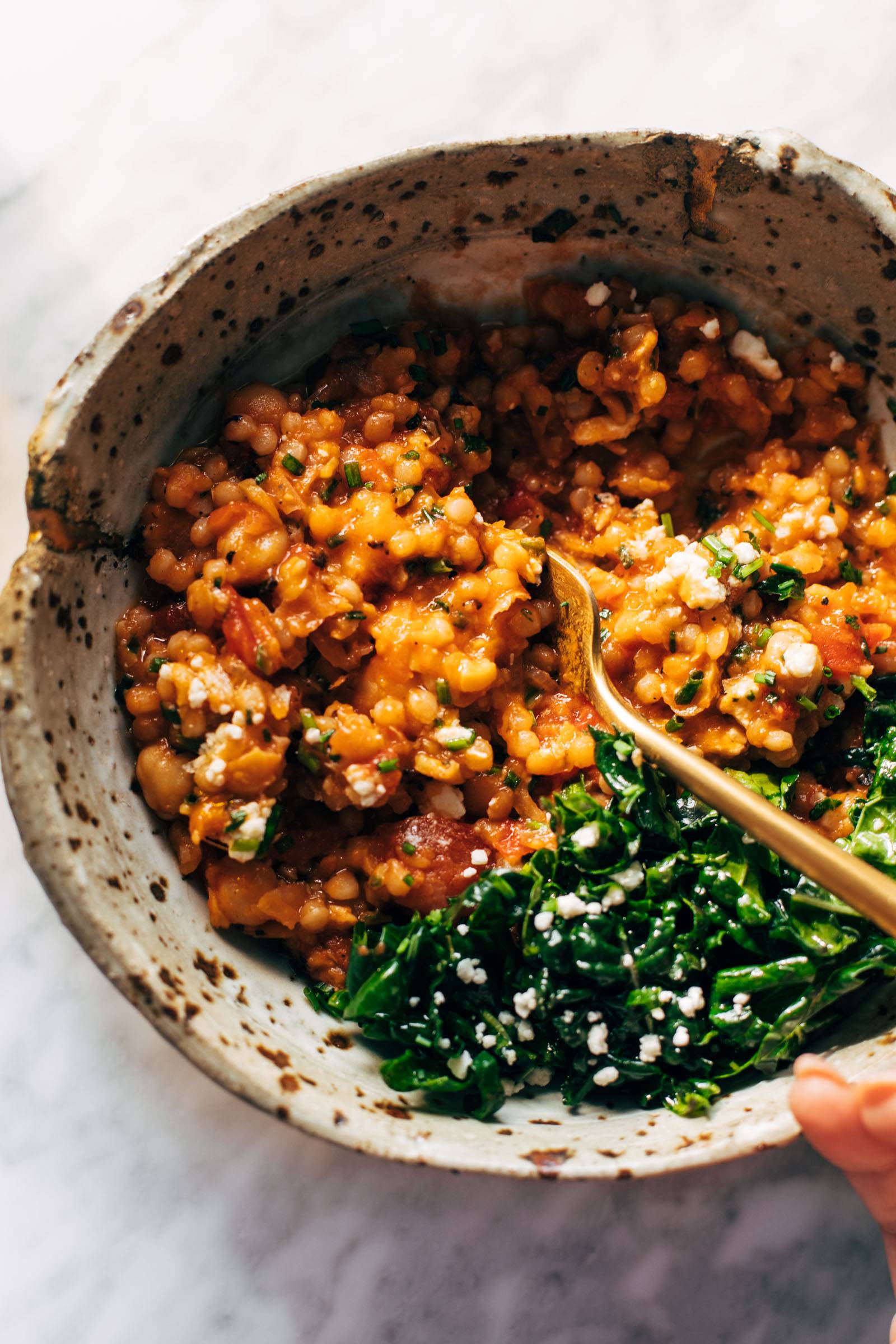 Couscous and tomatoes in a bowl with a spoon and kale.