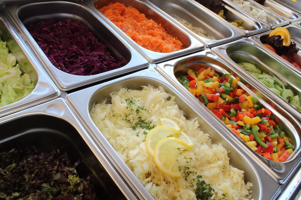 A self-service salad bar with trays of fresh vegetables