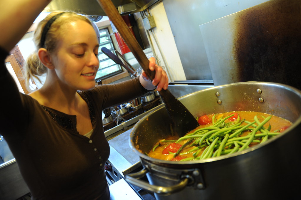 The cook's smile, cooking vegetarian green bean soup, big wooden paddle spoon, young woman in a brown shirt, p