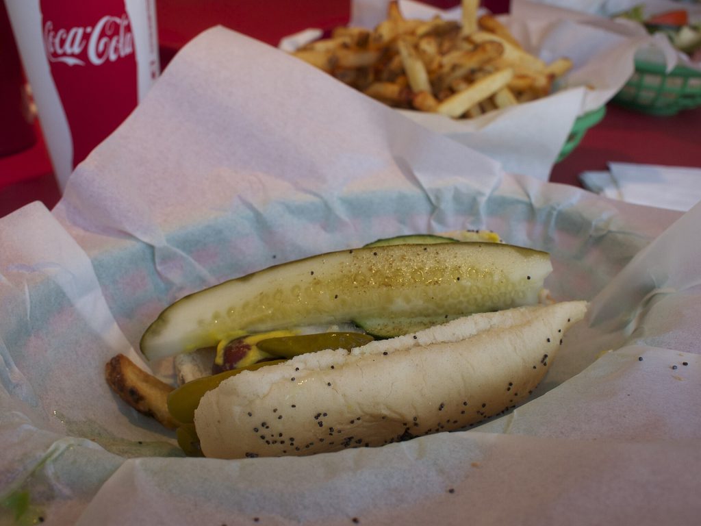 A Chicago-style hot dog with mustard, relish, tomato, pickle and sport peppers on a poppy seed bun