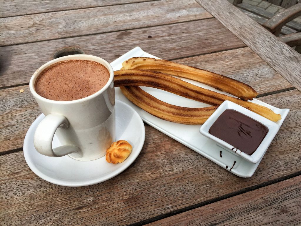 Churros dusted with sugar beside a cup of hot chocolate